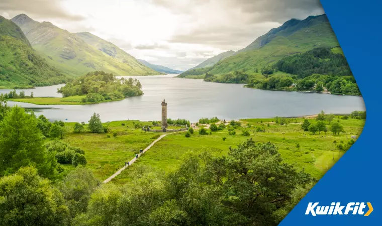 Vibrant green shores of Loch Lamond, with a large stone tower by the water.