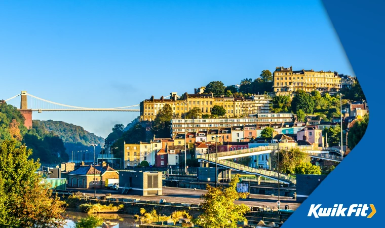 Houses o hill surrounded with greenery with a bridge in the background.