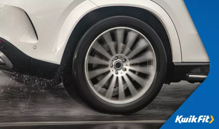 A close-up view of the spinning back tyre of a white RWD car driving in the rain.