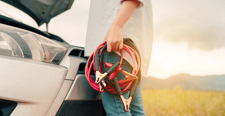 Person holding jump leads in front of open bonnet of car.