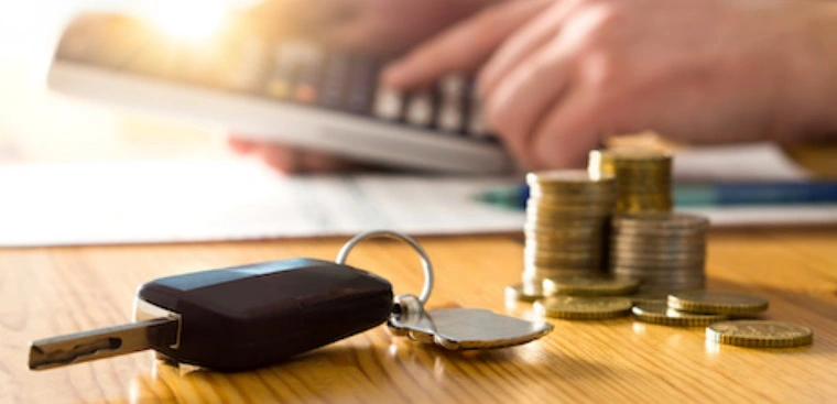 A man uses a calculator to work out his car tax while a set of car keys and piled up coins sit in the foreground.