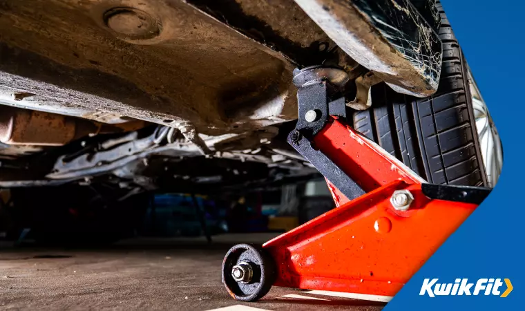 A red trolley jack holding up a corner of a car.