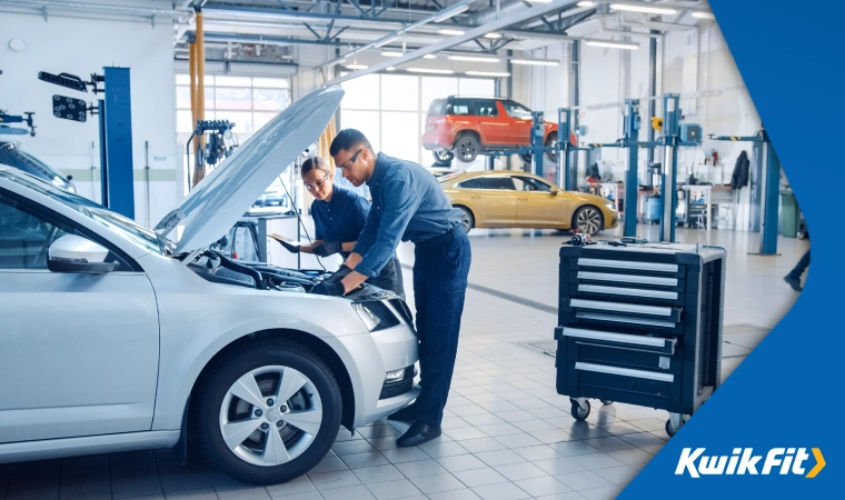 Two technicians examining under the bonnet of a car.