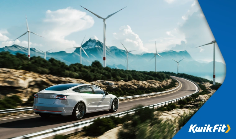 Modern electric vehicle driving on motorway in the mountains surrounded by a wind turbine farm.