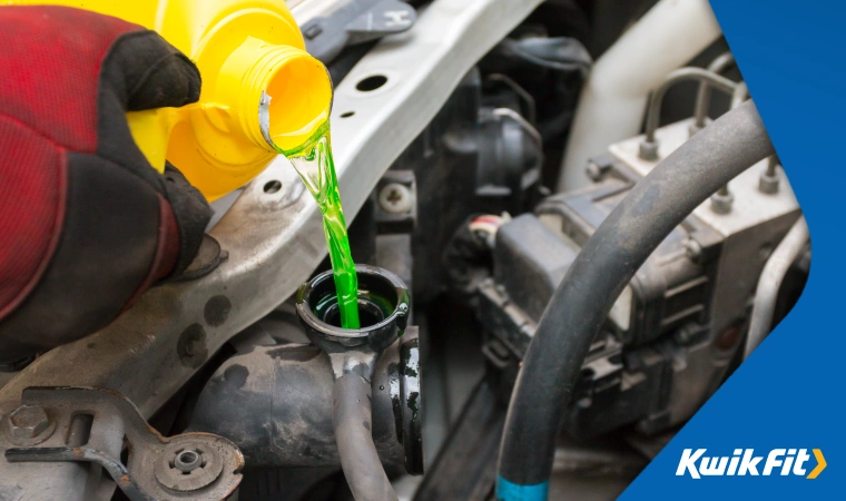 Close up of hands with gloves pouring green antifreeze into the coolant reservoir of a car.