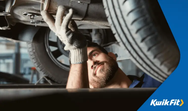 A technician looks under a car and checks an exhaust during an MOT.