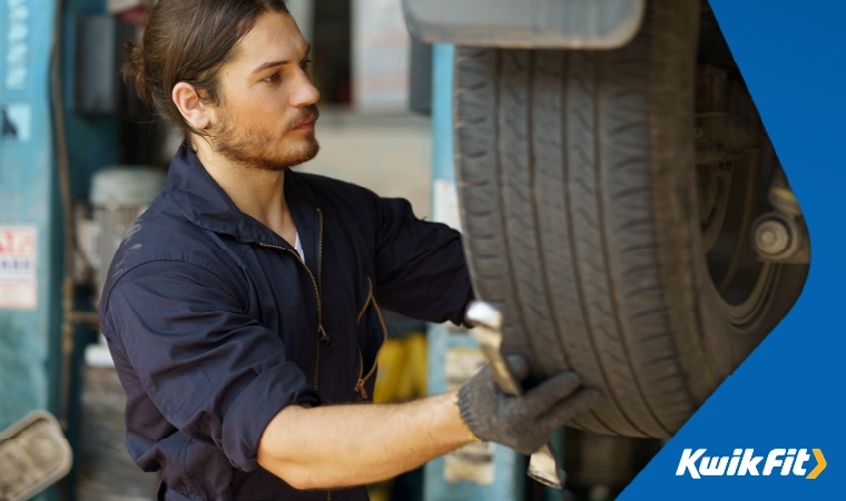 A mechanic changing a tyre on a vehicle that's lifted up in front of him.