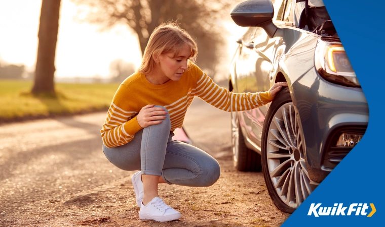 A person kneels down to check their tyre pressure at the side of a road.