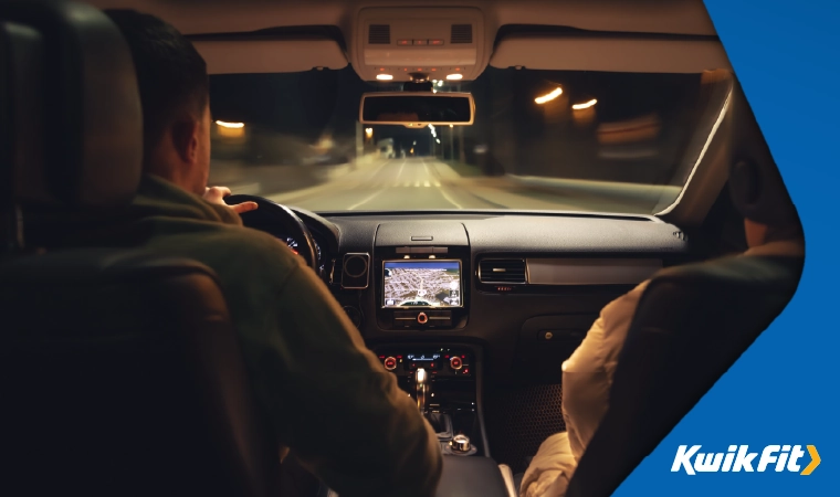 Two people sitting in the front of a car driving on a road at night.