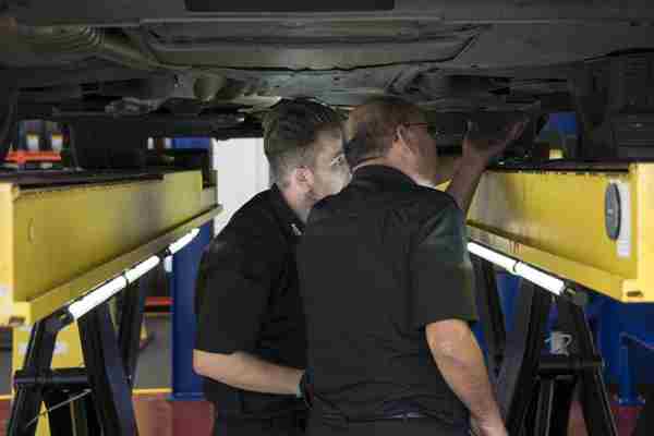 Two men standing under a car checking the fuel system